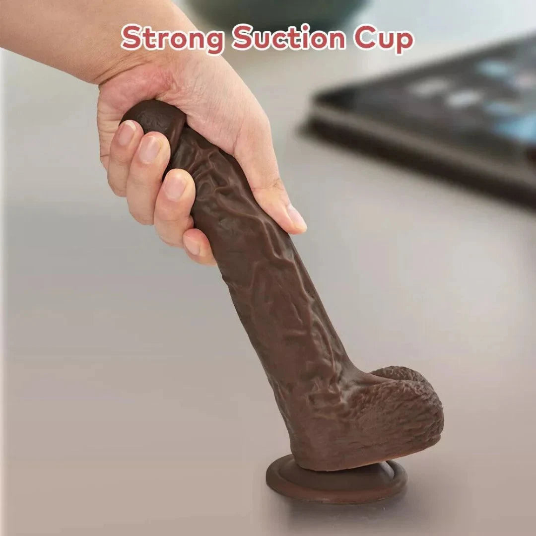 Hand holding a brown silicone dildo with a strong suction cup on a neutral background